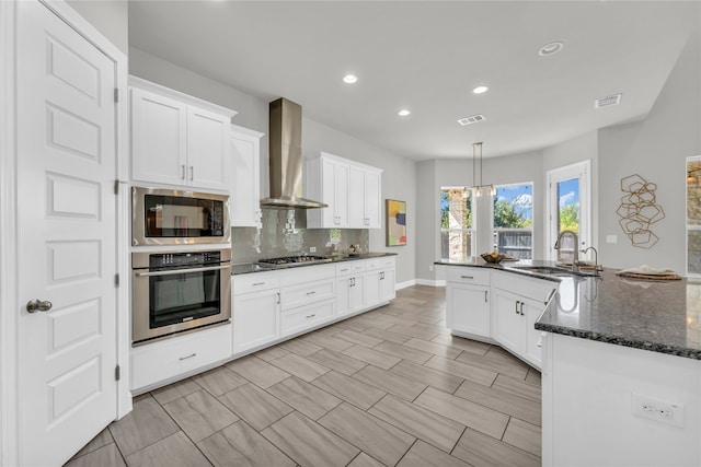 kitchen with white cabinetry, stainless steel appliances, wall chimney exhaust hood, and dark stone counters