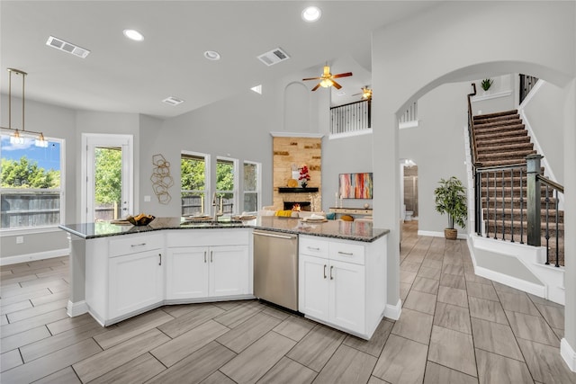 kitchen with hanging light fixtures, white cabinetry, high vaulted ceiling, stainless steel dishwasher, and dark stone counters