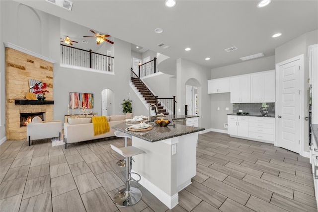 kitchen with an island with sink, white cabinetry, a kitchen bar, dark stone countertops, and a fireplace