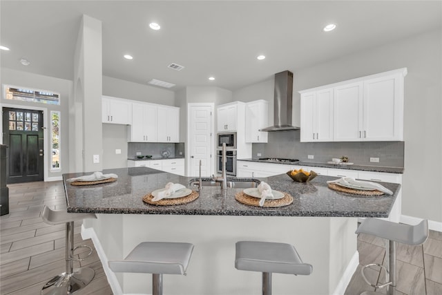 kitchen with a breakfast bar area, appliances with stainless steel finishes, white cabinetry, and wall chimney range hood