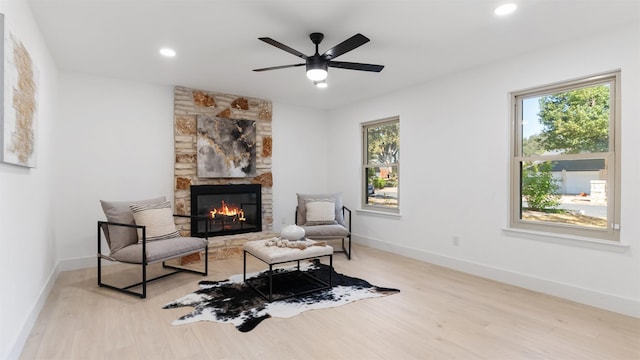 living area with ceiling fan, light hardwood / wood-style floors, and a stone fireplace