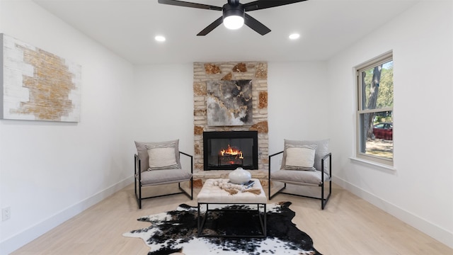 living area with ceiling fan, light wood-type flooring, and a stone fireplace