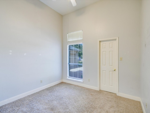 carpeted spare room featuring a towering ceiling and ceiling fan