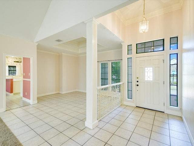 entrance foyer with crown molding, ornate columns, a chandelier, and light tile patterned floors