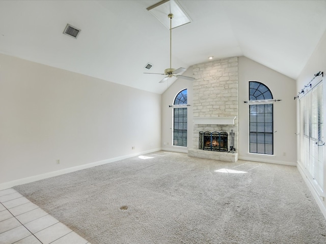 unfurnished living room with light carpet, ceiling fan, a barn door, high vaulted ceiling, and a fireplace