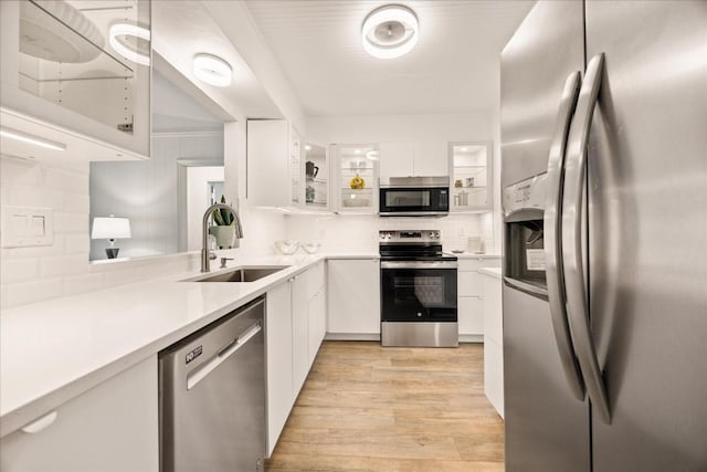 kitchen featuring appliances with stainless steel finishes, white cabinetry, sink, backsplash, and light hardwood / wood-style floors