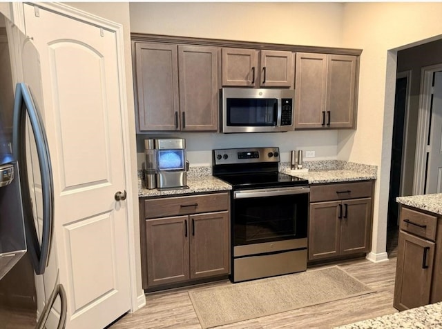 kitchen featuring light stone counters, appliances with stainless steel finishes, light wood-type flooring, and dark brown cabinets