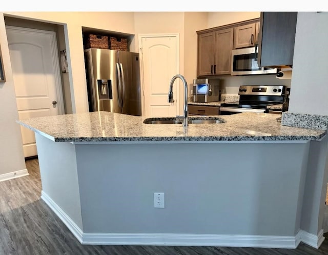 kitchen featuring kitchen peninsula, stainless steel appliances, sink, light stone counters, and dark hardwood / wood-style flooring