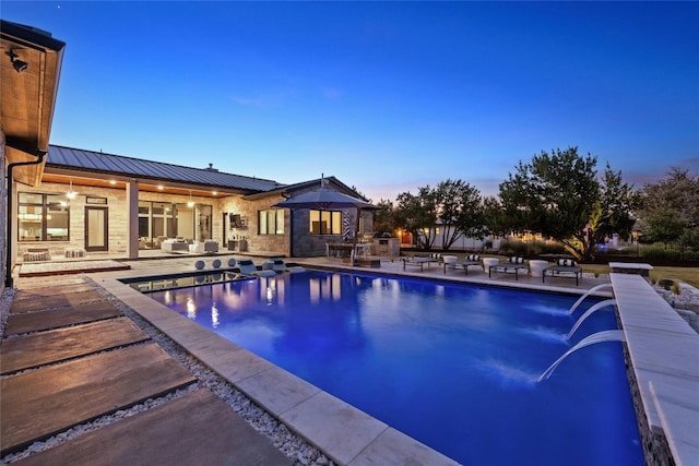 pool at dusk featuring a patio and pool water feature