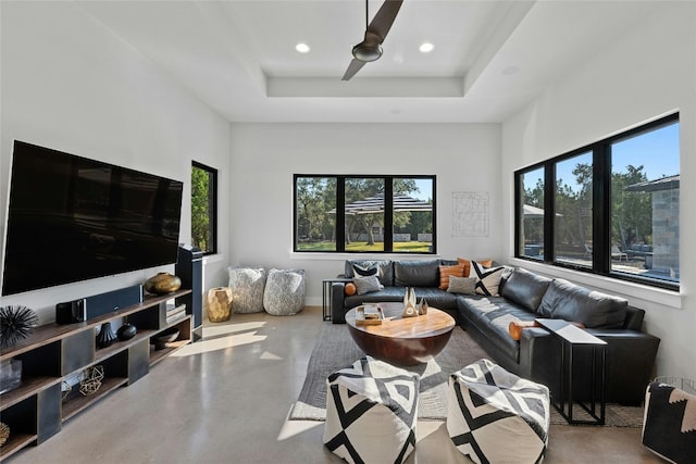 living room featuring a wealth of natural light, ceiling fan, concrete floors, and a raised ceiling