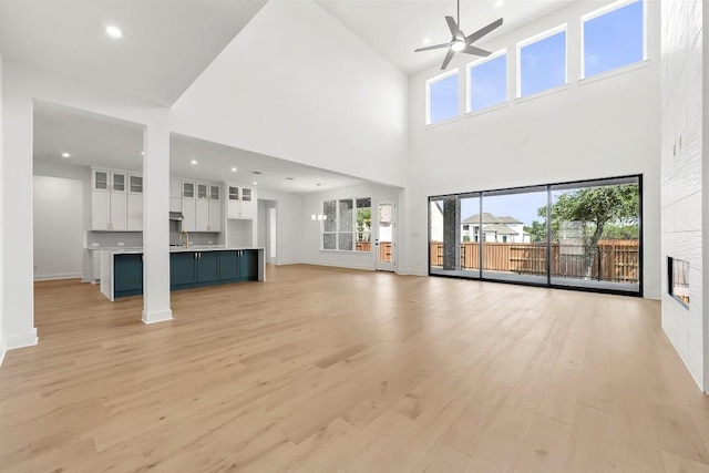 2305 Shane Ranch Dr, Cedar Park, TX 78641 - unfurnished living room featuring a ceiling fan, light wood-style flooring, a high ceiling, a glass covered fireplace, and recessed lighting