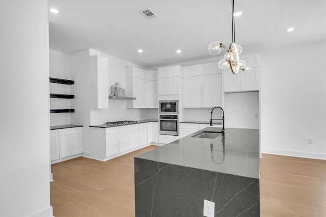 kitchen with white cabinets, light wood-type flooring, dark stone counters, stainless steel appliances, and sink