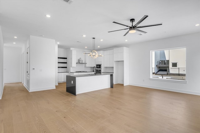 kitchen with stainless steel microwave, a center island with sink, pendant lighting, white cabinets, and light hardwood / wood-style floors