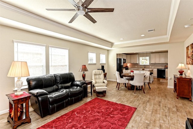 living room with ornamental molding, a tray ceiling, ceiling fan, sink, and light hardwood / wood-style flooring