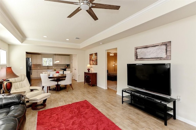 living room with a tray ceiling, ceiling fan, light hardwood / wood-style flooring, and crown molding