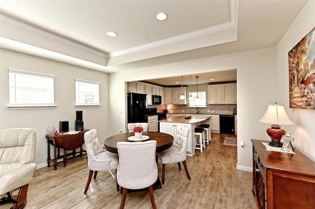 dining area featuring light wood-type flooring, a tray ceiling, crown molding, and sink