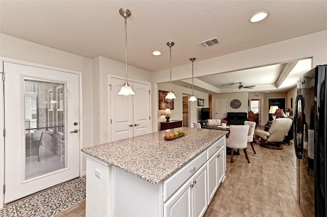 kitchen with white cabinetry, ceiling fan, pendant lighting, a tray ceiling, and black refrigerator