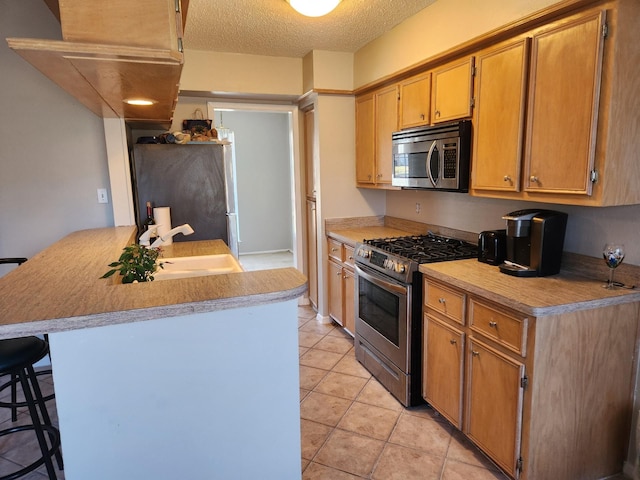 kitchen with a kitchen bar, sink, a textured ceiling, kitchen peninsula, and stainless steel appliances