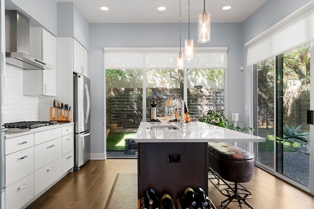 kitchen with white cabinets, appliances with stainless steel finishes, wall chimney exhaust hood, an island with sink, and sink