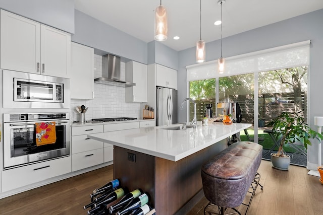 kitchen with white cabinets, a kitchen island with sink, wall chimney range hood, and stainless steel appliances