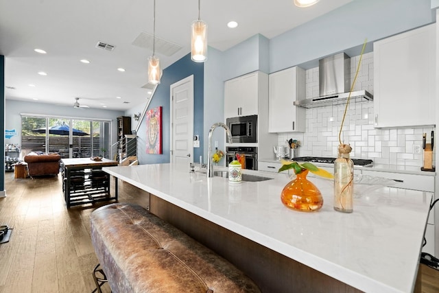 kitchen with wall chimney exhaust hood, white cabinetry, backsplash, pendant lighting, and appliances with stainless steel finishes