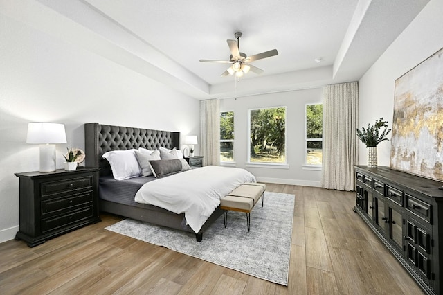 bedroom with a raised ceiling, light wood-type flooring, and ceiling fan