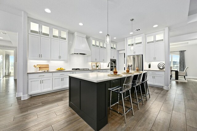 kitchen featuring custom exhaust hood, white cabinetry, a kitchen island with sink, and high end fridge