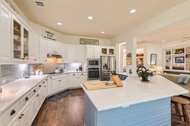 kitchen with a center island, dark wood-type flooring, a kitchen breakfast bar, white cabinets, and appliances with stainless steel finishes