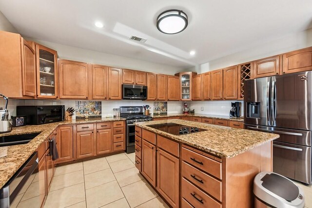 kitchen featuring appliances with stainless steel finishes, light tile patterned flooring, light stone countertops, and a center island