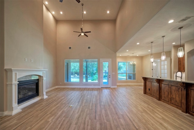 unfurnished living room featuring light hardwood / wood-style flooring, a towering ceiling, and ceiling fan