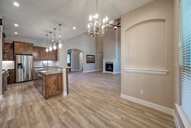 kitchen with light wood-type flooring, appliances with stainless steel finishes, pendant lighting, and an island with sink