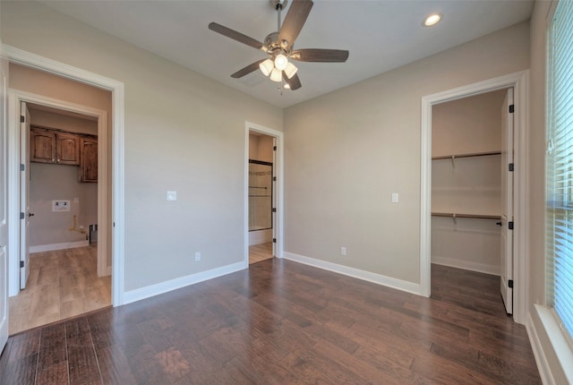 unfurnished bedroom featuring a walk in closet, a closet, dark wood-type flooring, and ceiling fan