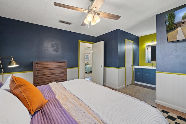 bedroom with a textured ceiling, ceiling fan, sink, light tile patterned floors, and connected bathroom