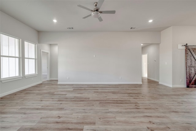 unfurnished room with ceiling fan, light hardwood / wood-style flooring, and a barn door