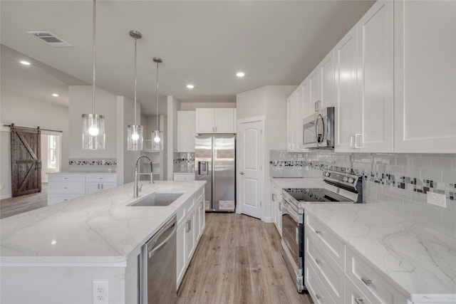 kitchen with white cabinets, an island with sink, sink, pendant lighting, and stainless steel appliances