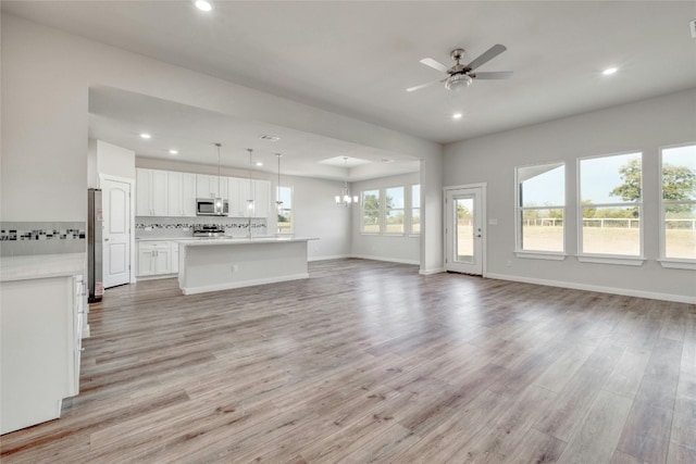 unfurnished living room with sink, ceiling fan with notable chandelier, and light wood-type flooring