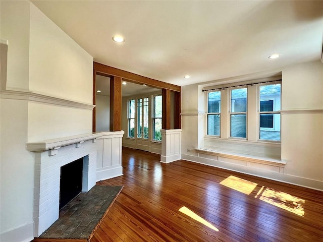 unfurnished living room featuring a brick fireplace, wood-type flooring, baseboards, and recessed lighting