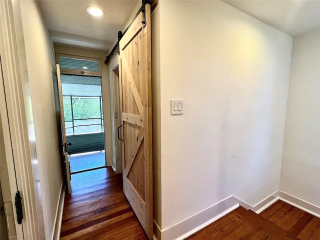 hall featuring a barn door, dark wood finished floors, and baseboards