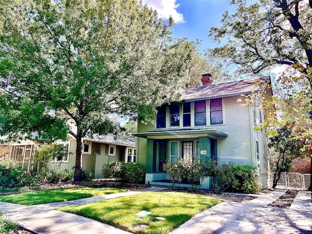 american foursquare style home with a front lawn, a chimney, and fence