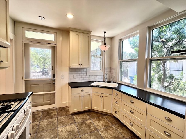 kitchen featuring decorative light fixtures, gas range oven, dark countertops, backsplash, and a sink