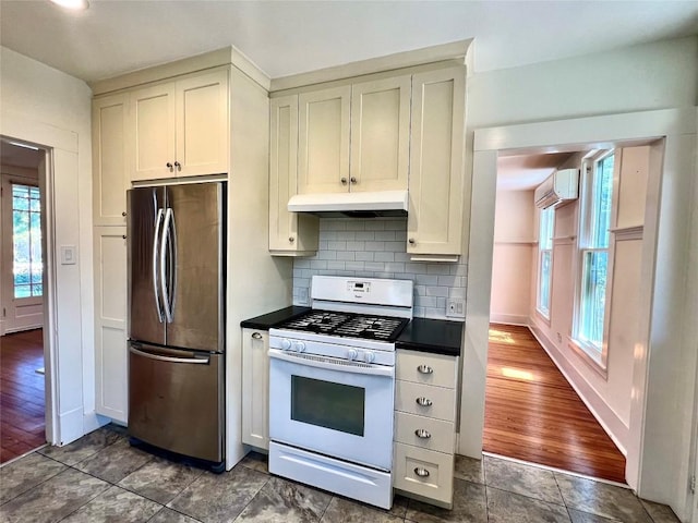 kitchen featuring under cabinet range hood, a wall mounted AC, freestanding refrigerator, white gas range, and dark countertops