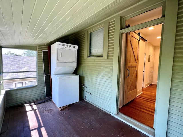 laundry area featuring stacked washer and dryer, a barn door, laundry area, dark wood finished floors, and wood ceiling