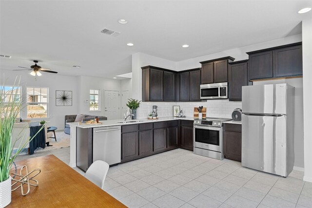 kitchen with dark brown cabinets, kitchen peninsula, ceiling fan, stainless steel appliances, and decorative backsplash