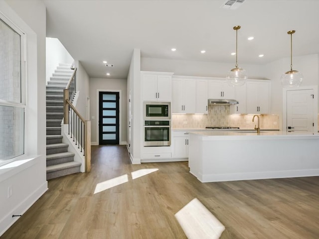 kitchen featuring pendant lighting, white cabinetry, black microwave, and stainless steel oven