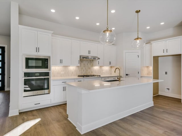 kitchen with white cabinetry, sink, stainless steel appliances, an island with sink, and decorative light fixtures