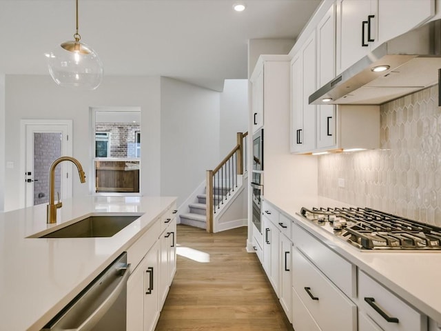 kitchen with sink, light wood-type flooring, appliances with stainless steel finishes, decorative light fixtures, and white cabinetry