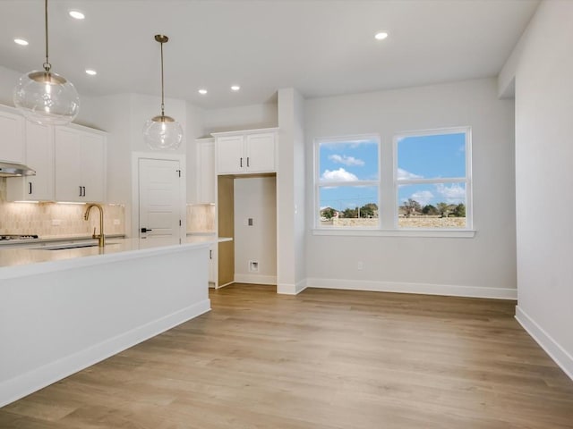 kitchen featuring white cabinetry, sink, gas stovetop, range hood, and pendant lighting