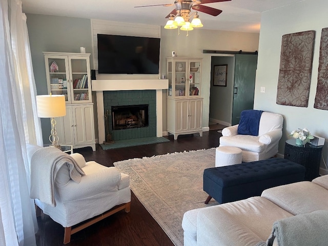 living room featuring ceiling fan, a fireplace, dark hardwood / wood-style flooring, and a barn door