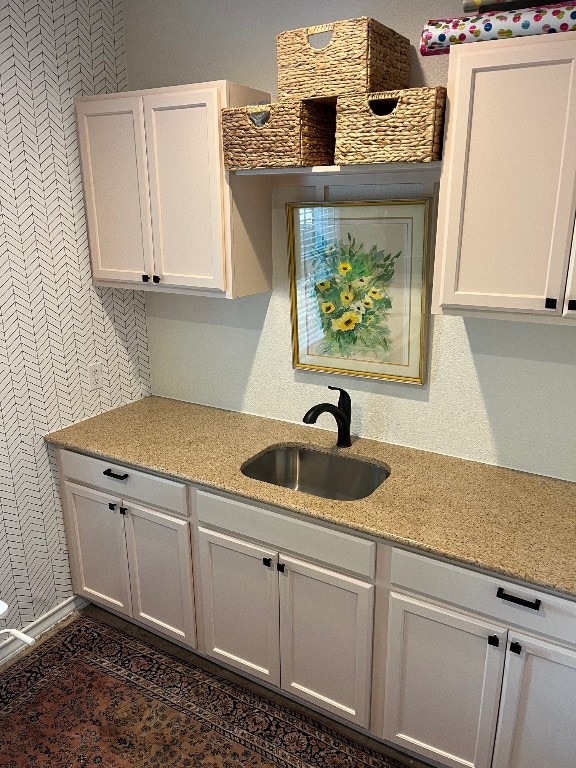 kitchen with light stone countertops, sink, and white cabinets