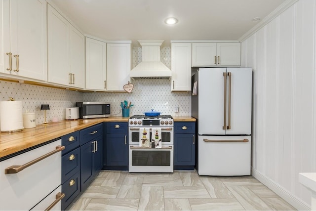 kitchen with white appliances, white cabinetry, custom exhaust hood, wooden counters, and blue cabinetry